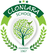Emblem der Clonlara School: grüner Baum mit fliegender Taube in weißem Schild, umgeben von Lorbeerkranz; darüber Banner mit Aufschrift ‚Clonlara School‘, unten Zusatz ‚Founded 1967‘.