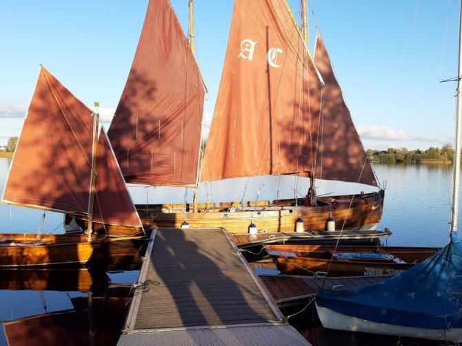 Holz-Segelkutter mit drei rostroten Gaffelsegeln liegt an einem Steg im Abendlicht; Aufnahme zeigt Ausbildungsboot eines Erziehungsschiff-Programms.