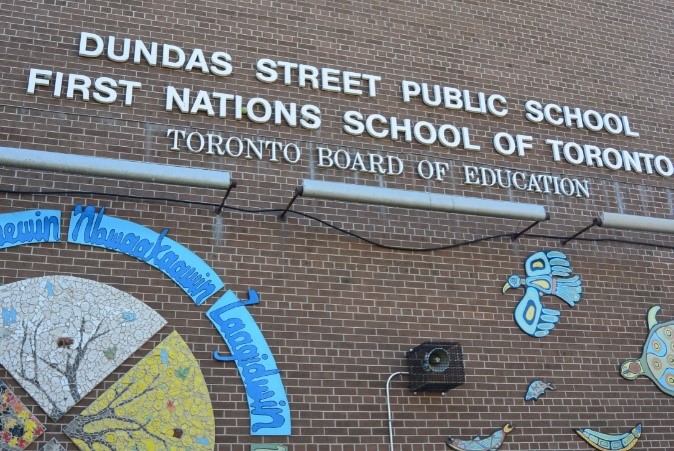 Backsteinfassade mit weißer Aufschrift ‚Dundas Street Public School – First Nations School of Toronto‘ und farbigen indigenen Mosaiken.